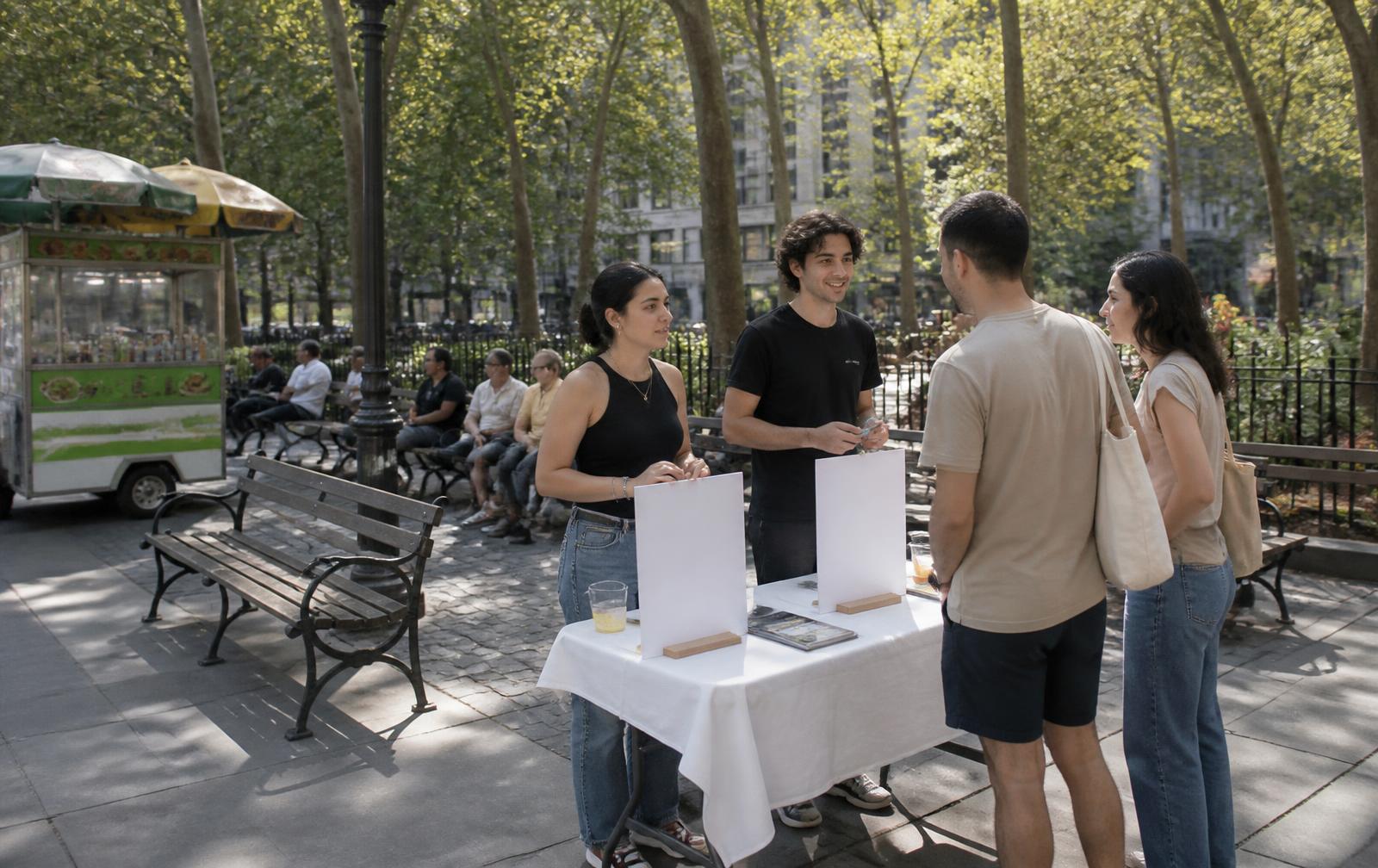 Two staff members talking with passersby at an outdoor table in a New York plaza