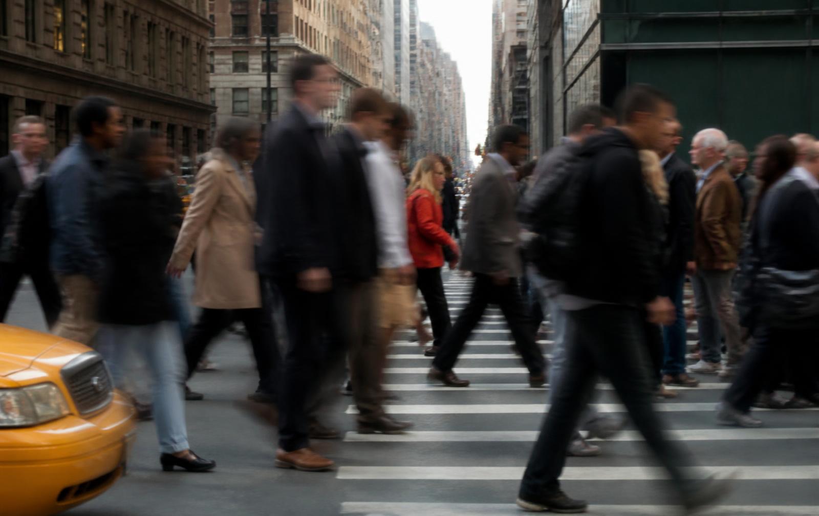 Commuters crossing a Manhattan intersection in heavy motion blur beside a yellow taxi